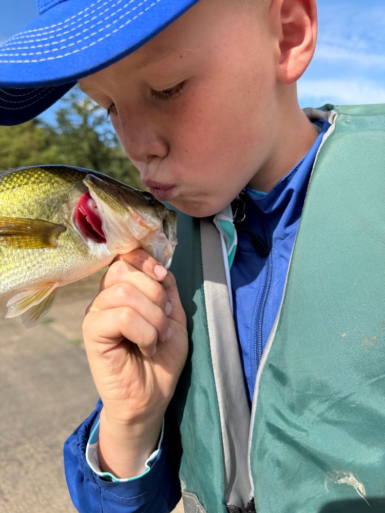 A boy in a blue cap kissing a largemouth bass